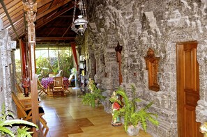 A room with a stone wall, wooden furniture, and hanging decorations. - Aahh Bali Bed and Breakfast (Jimbaran)