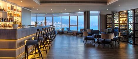 A bar area with a view of the city, wooden flooring, and a chandelier.