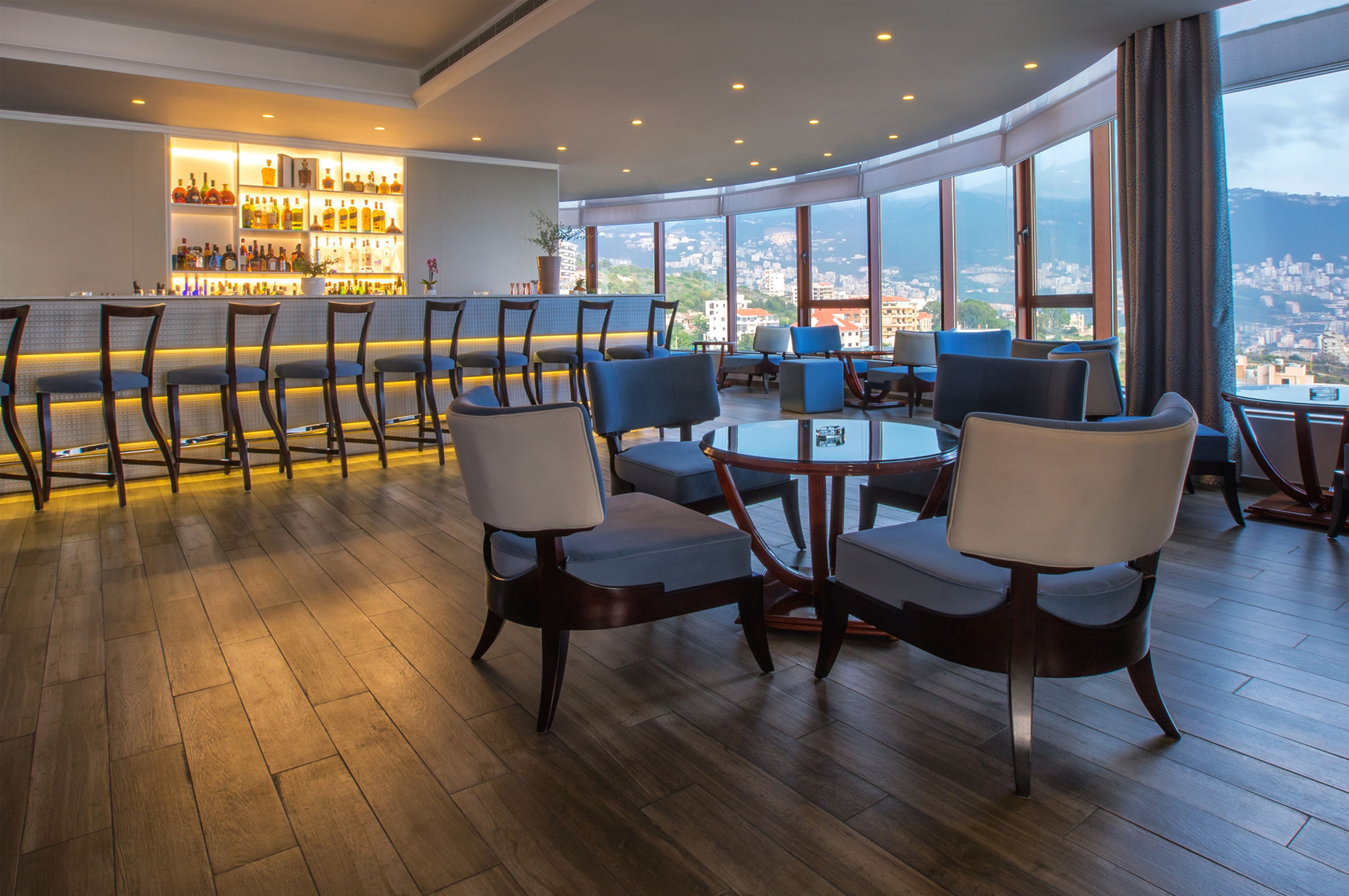 A bar area with a view of the city, wooden flooring, and modern seating.