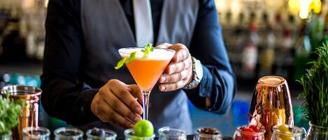 A bartender holding a cocktail with various garnishes and ingredients on a bar counter.