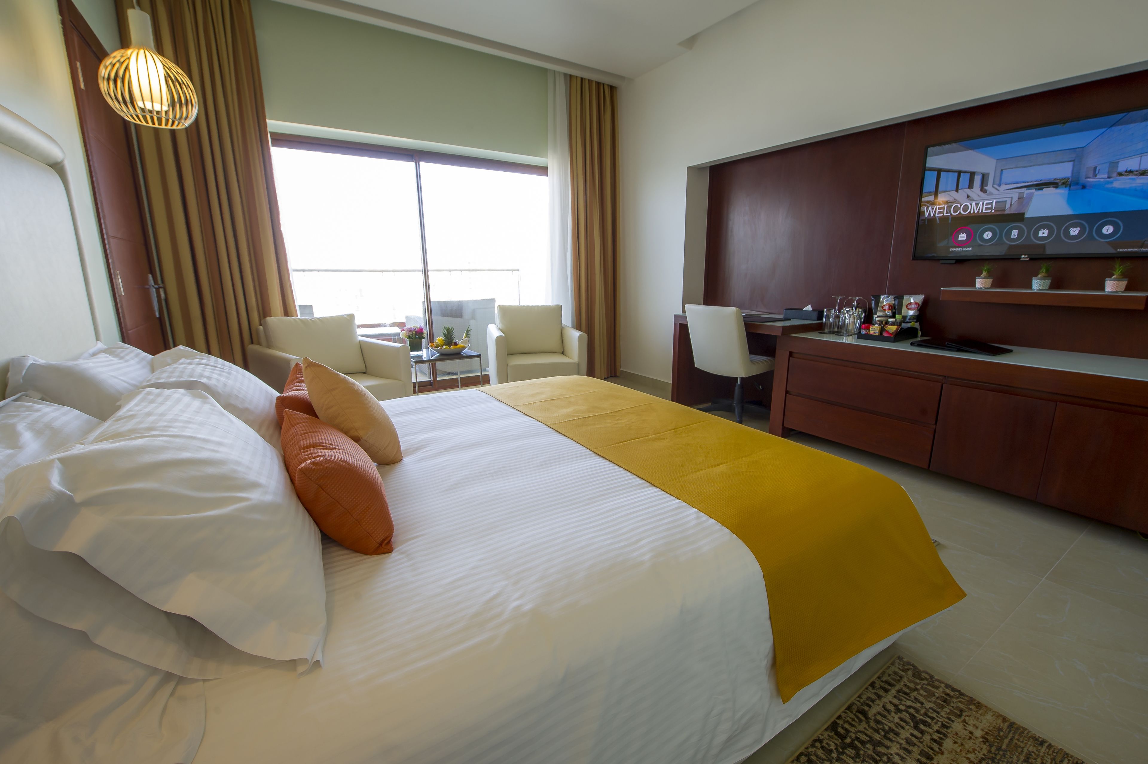 Quarto de hotel com cama, escrivaninha, televisão e vista para o exterior.