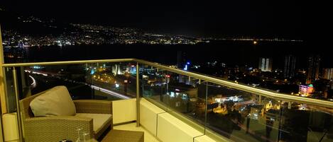 Un balcón con baranda de vidrio que da a una vista nocturna de la ciudad.