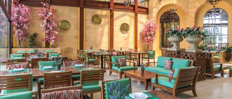Un restaurante amplio con mesas y sillas de madera, asientos acolchados verdes y plantas decorativas.