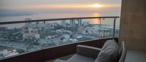 A balcony with wicker furniture and a view of a cityscape during sunset.