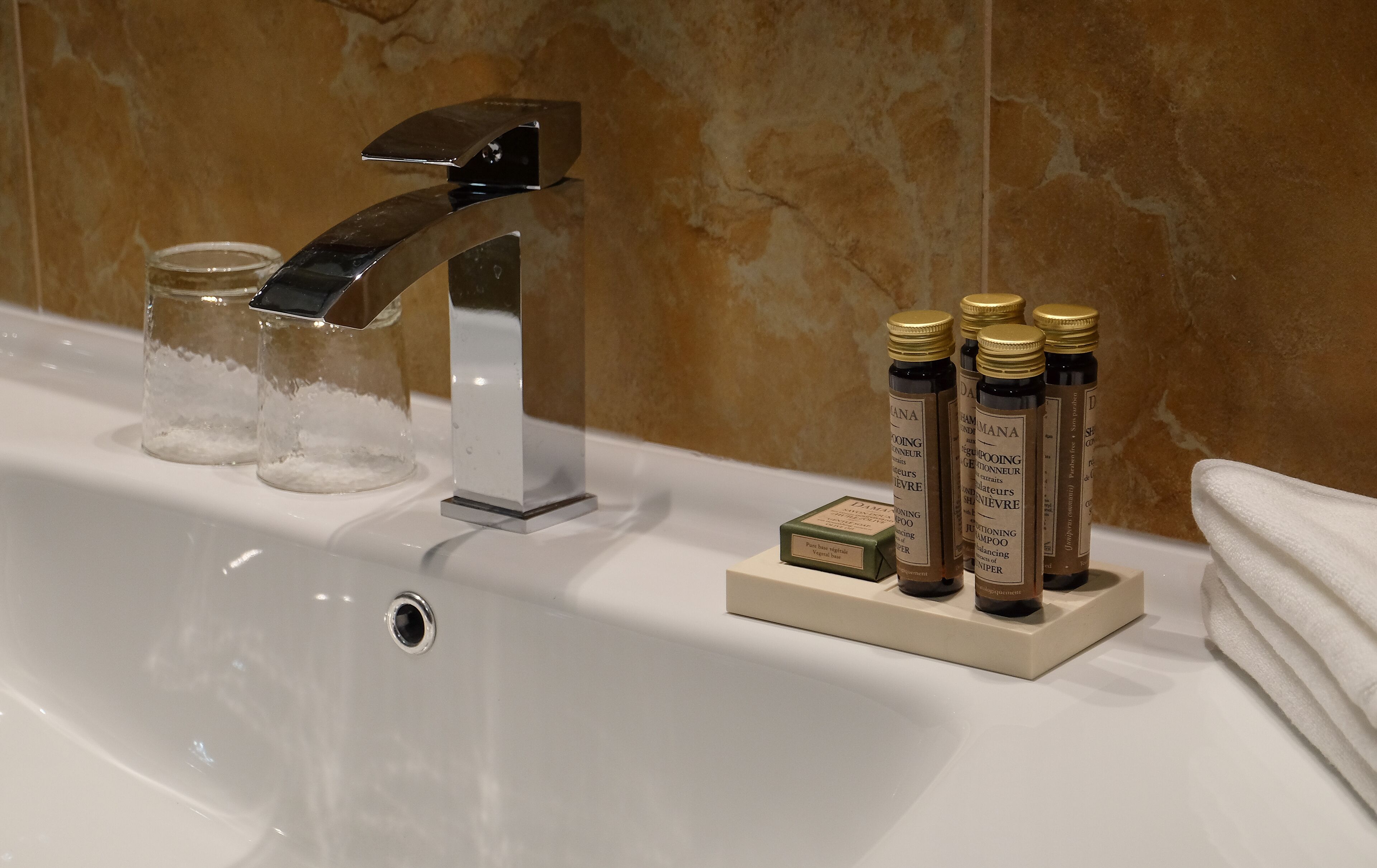 A bathroom sink with a modern faucet, clear glass containers, and bottles of shampoo.