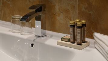 A bathroom sink with a modern faucet, clear glass containers, and bottles of shampoo.
