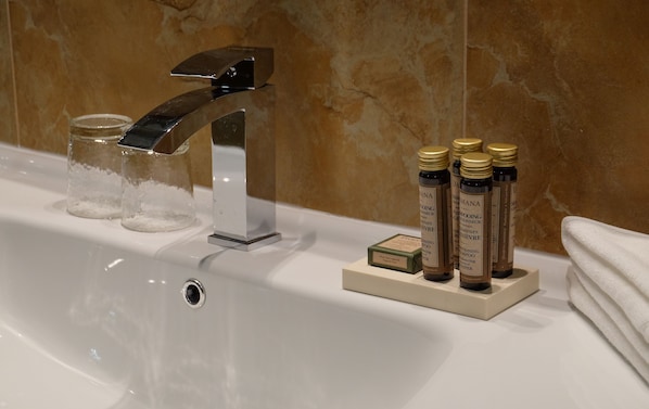 A bathroom sink with a modern faucet, clear glass containers, and bottles of shampoo.
