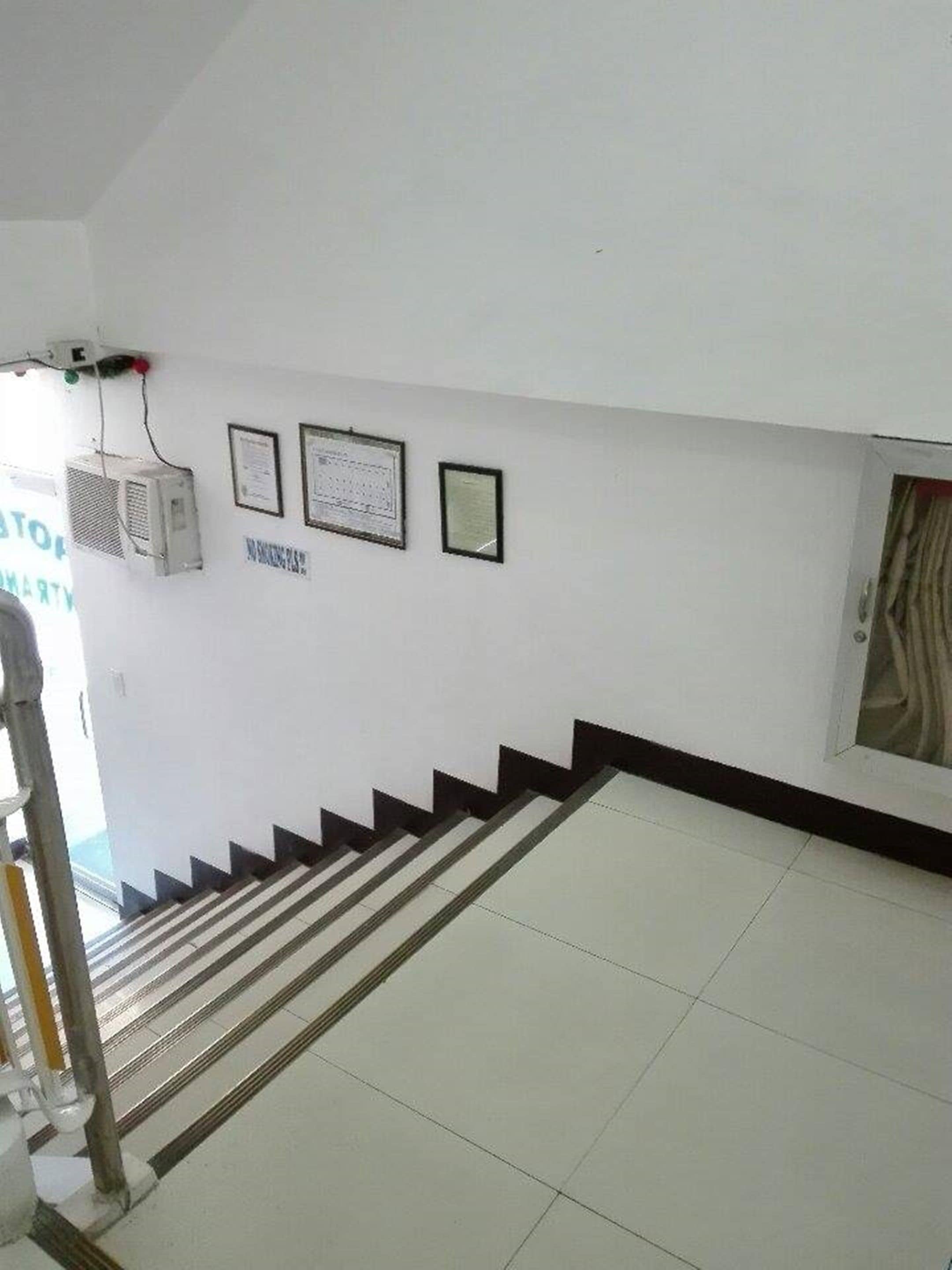 A staircase with a handrail leading to a landing. There are air conditioning units mounted on the wall and framed certificates or documents displayed above.