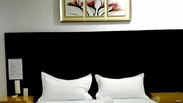 Een net opgemaakt bed met witte lakens en twee opgerolde handdoeken, een zwart hoofdeinde en een ingelijst kunstwerk erboven.