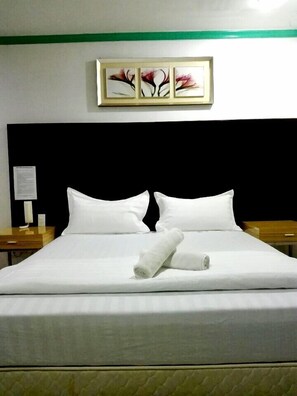A neatly made bed with white linens and two rolled towels, a black headboard, and a framed artwork above the bed. - Asia Novo Boutique Hotel - Kalibo (Kalibo)