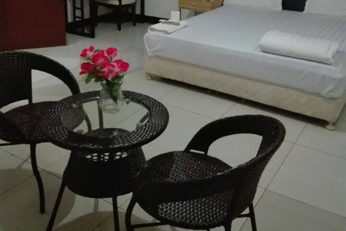Habitación de hotel con cama, escritorio, dos sillas, una mesita con flores y un cuadro en la pared.