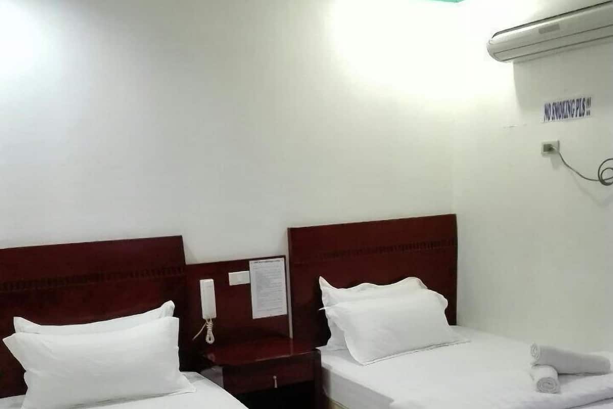 Habitación de hotel con dos camas, cada una con ropa de cama blanca y toallas enrolladas. Se aprecia un cabecero de madera, una mesita de noche y un equipo de aire acondicionado de pared con un letrero que dice 'NO FUMAR'.