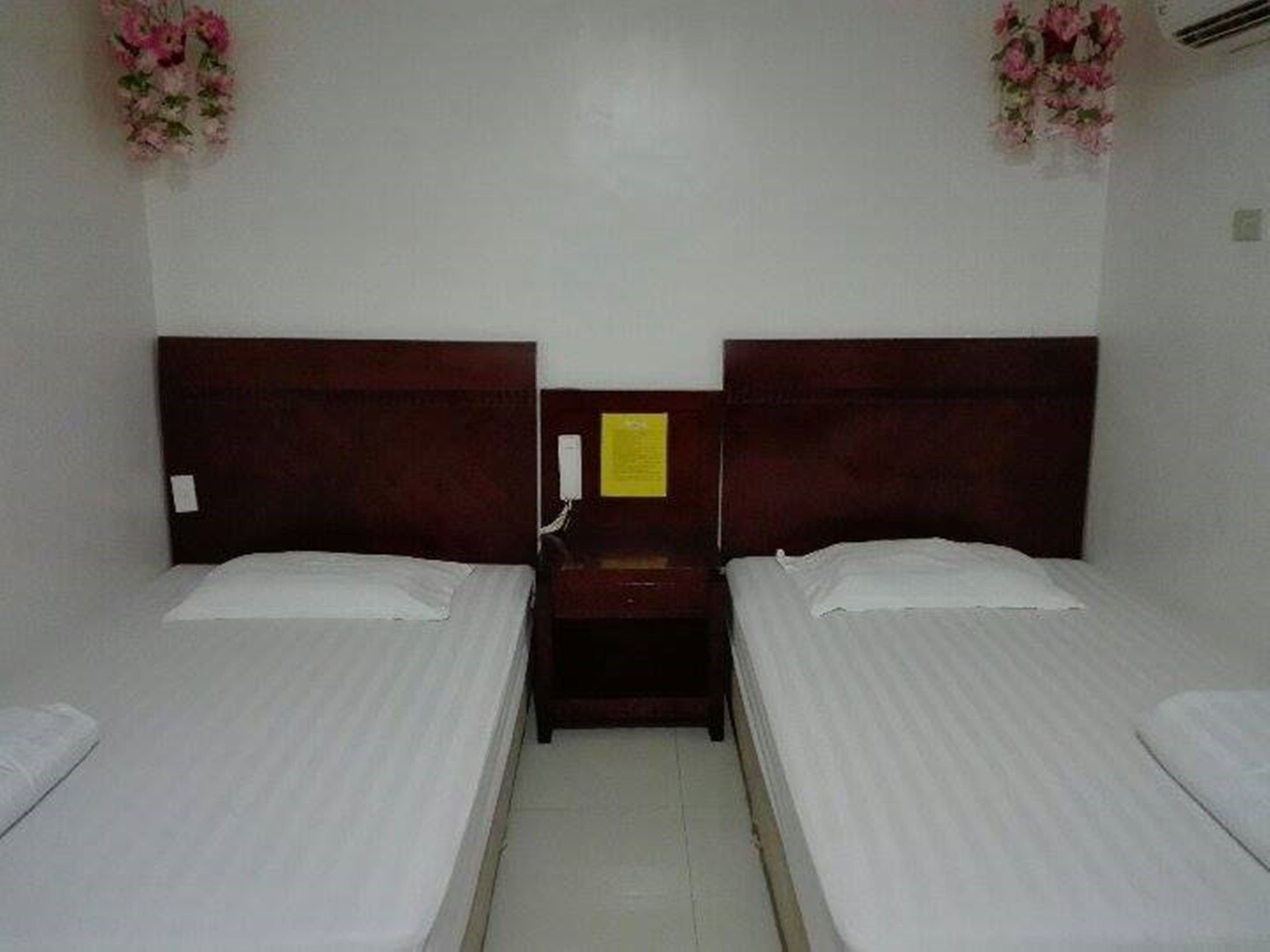 A room with two single beds, a wooden headboard, a nightstand, and a wall-mounted telephone.