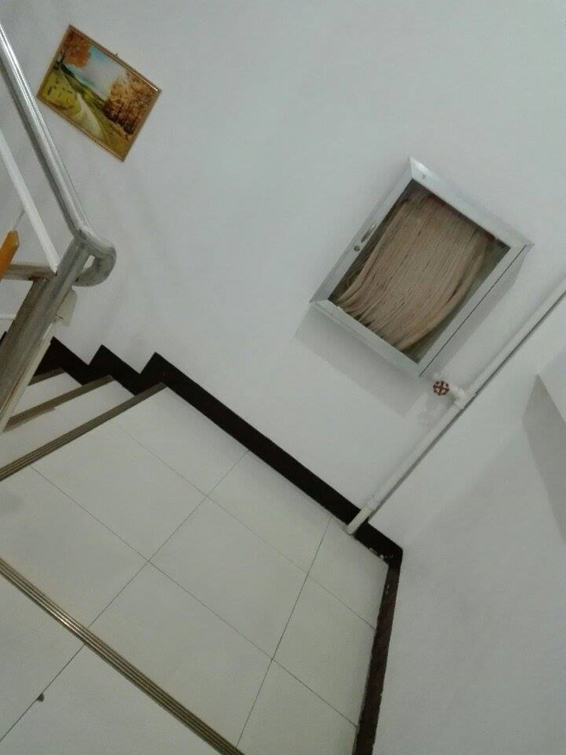 A staircase with a handrail, a small window with a curtain, and a picture on the wall.