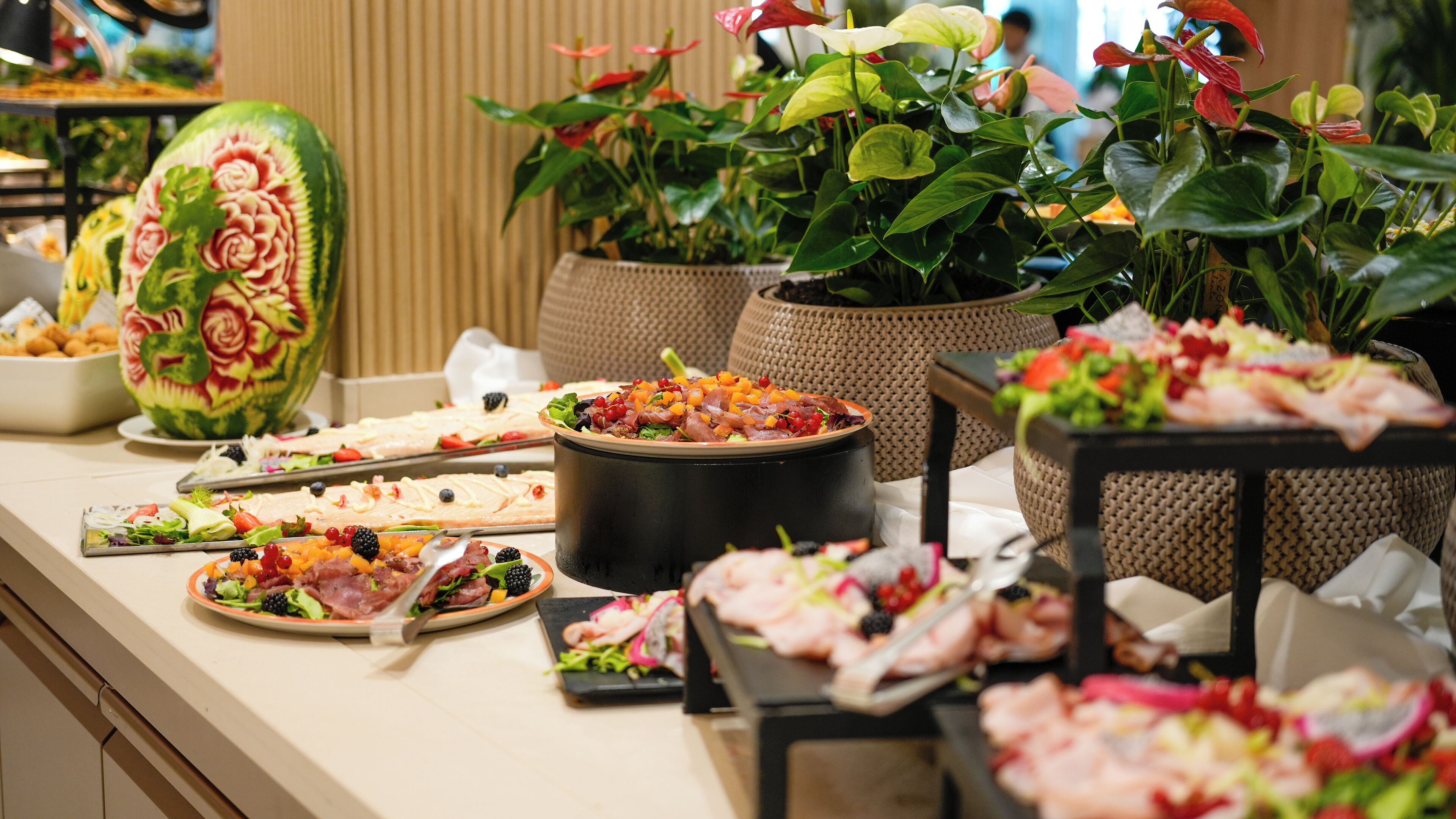 A buffet table with various dishes, including salads, meats, and a large watermelon carving.