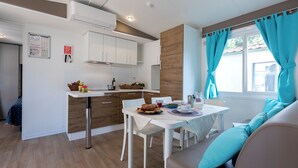 Une cuisine de taille réduite avec des meubles blancs, une table à manger avec des chaises et une fenêtre agrémentée de rideaux turquoise.