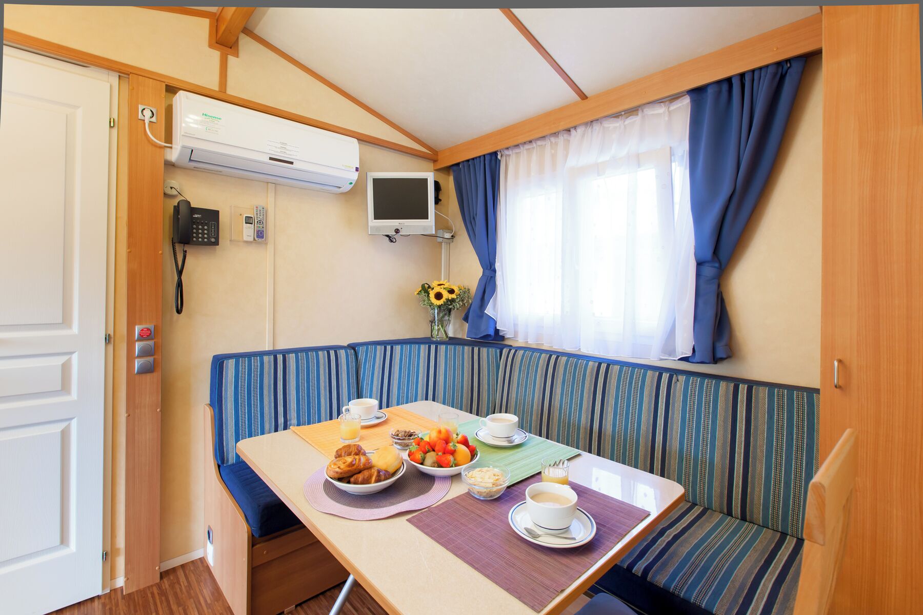 A compact room with a kitchenette, a dining area with a table set for breakfast, a sofa, and a window with curtains.
