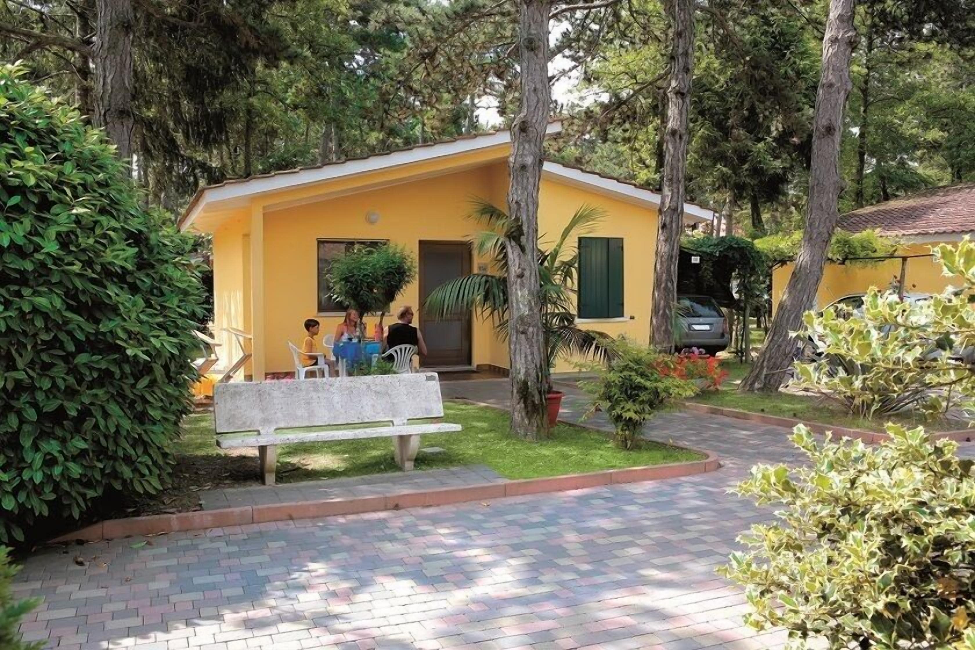 Um edifício amarelo com entrada pavimentada e um banco na frente.