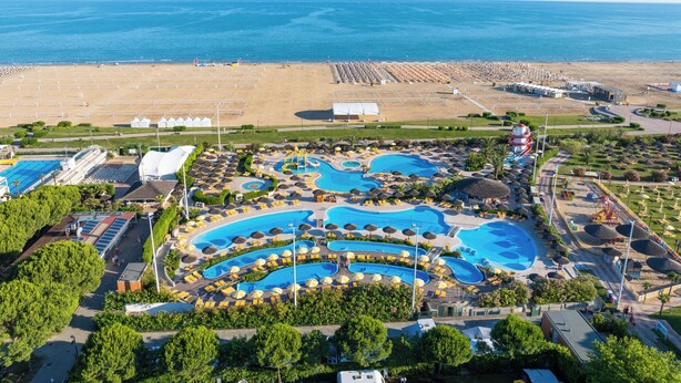 Vue aérienne d’un complexe hôtelier doté de plusieurs piscines, d’une plage et d’un grand bâtiment.