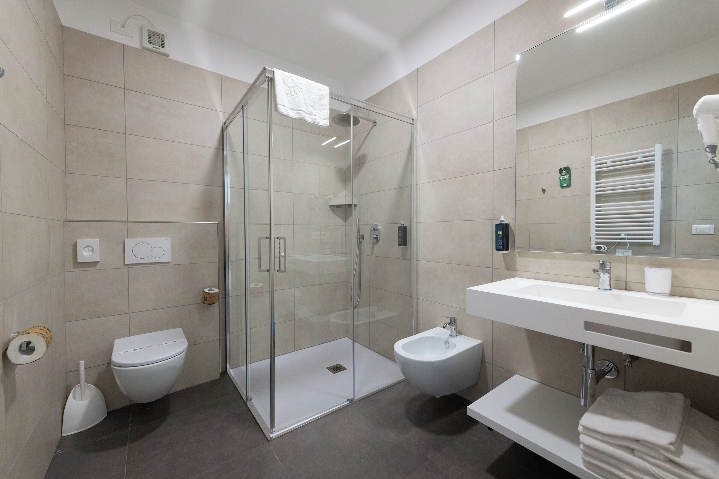 Un bagno moderno con doccia vetro, toilette, bidet e lavabo con specchio.