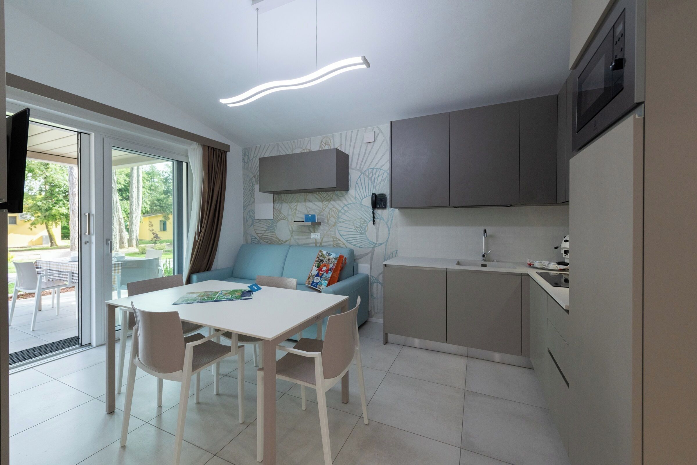 A compact kitchen with a dining area, a sofa, and a TV mounted on the wall.