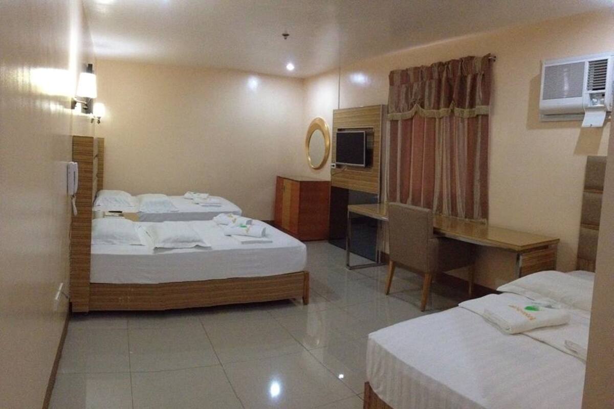 A hotel room with two beds, a desk, a chair, a TV, and an air conditioning unit.