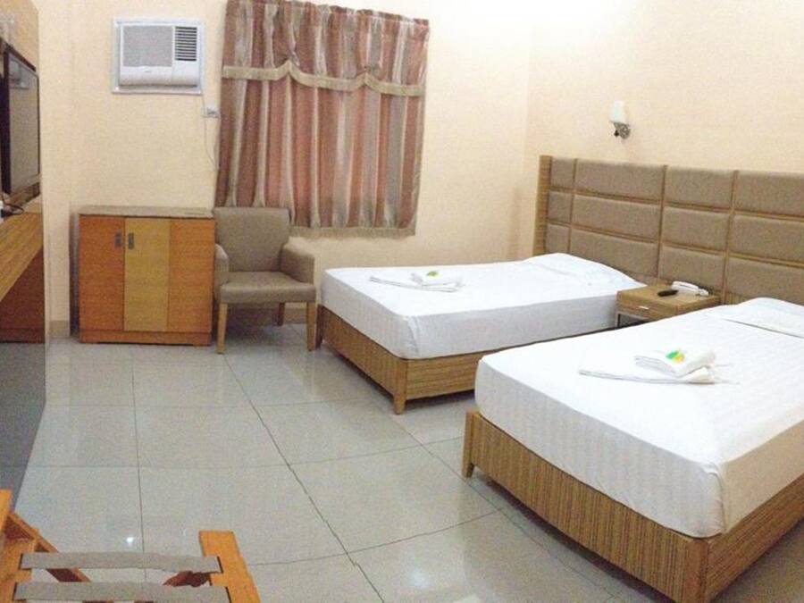 Habitación de hotel con dos camas individuales, un armario de madera, un escritorio, una silla y una ventana con cortinas.