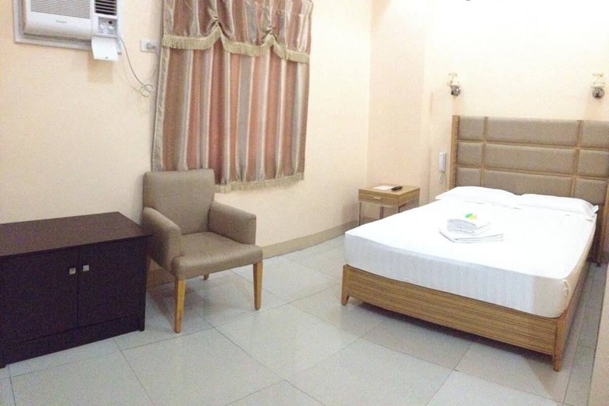 A hotel room with a bed, a chair, a small table, and a wardrobe.