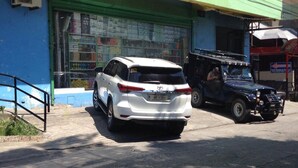 Un SUV blanco estacionado frente a un edificio con fachada verde y azul.