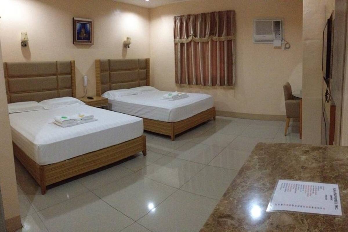 A hotel room with two single beds, a marble table, a chair, a TV, an air conditioning unit, and a framed picture on the wall.