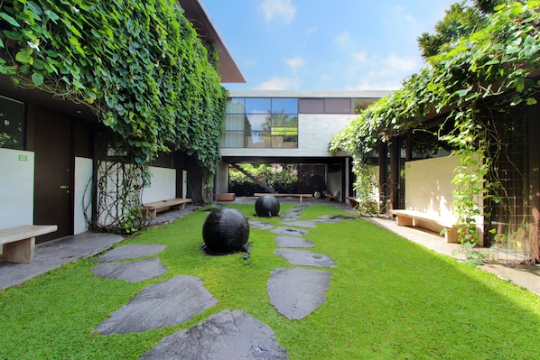 A courtyard with stone pathways, benches, and a grassy area. - Clio Apartments (Seminyak)