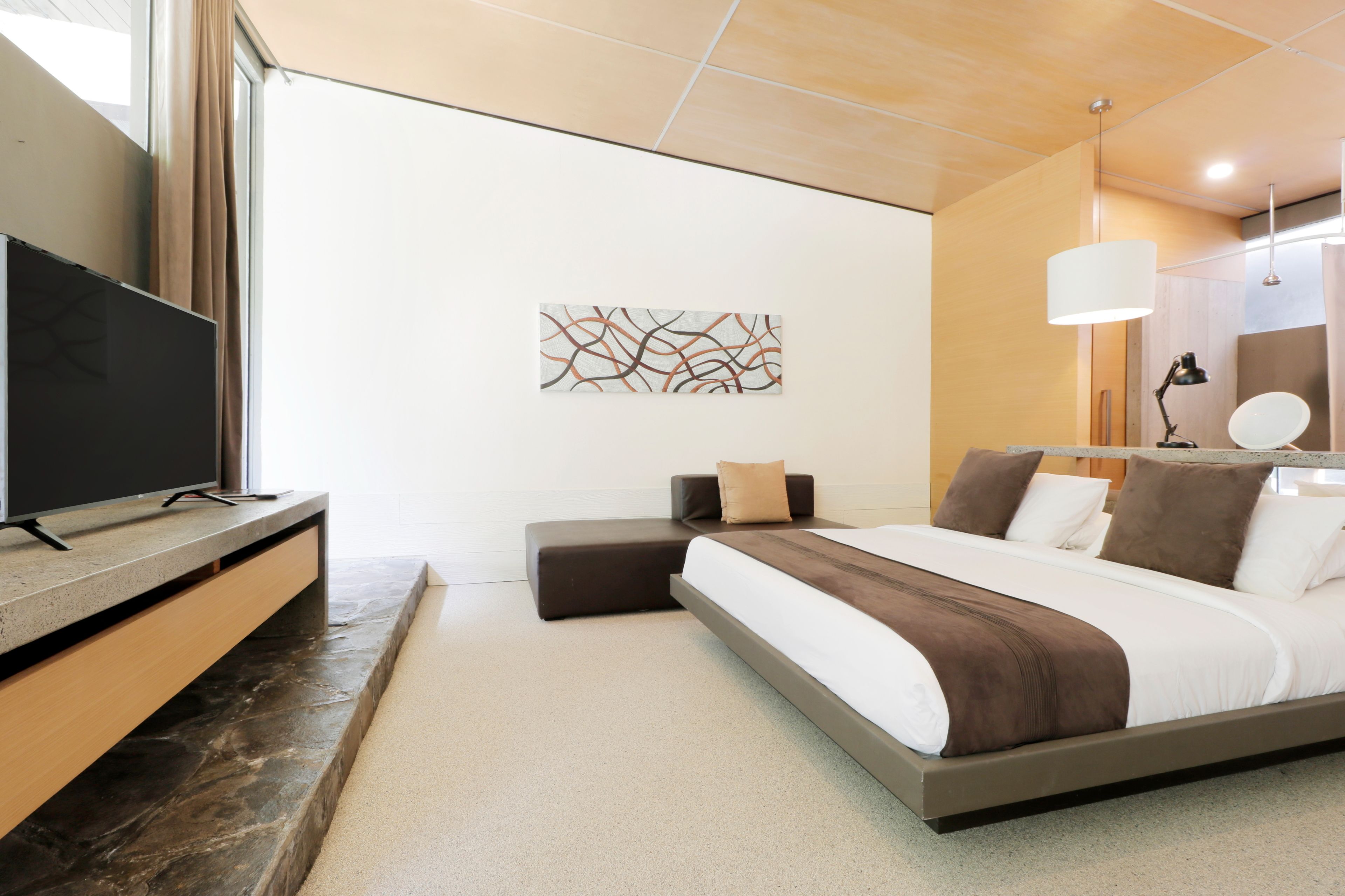 Een moderne slaapkamer met een groot bed, een televisie op een houten dressoir, een wanddecoratie in abstractie en een nachtkastje met een lamp.