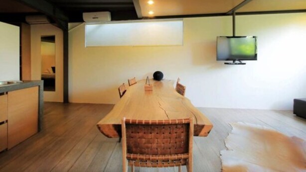 Una mesa de comedor de madera con sillas, un televisor montado y un tapete de piel en el suelo.