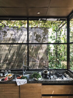 A kitchen with a large window, a sink, and a stove. - Clio Apartments (Seminyak)