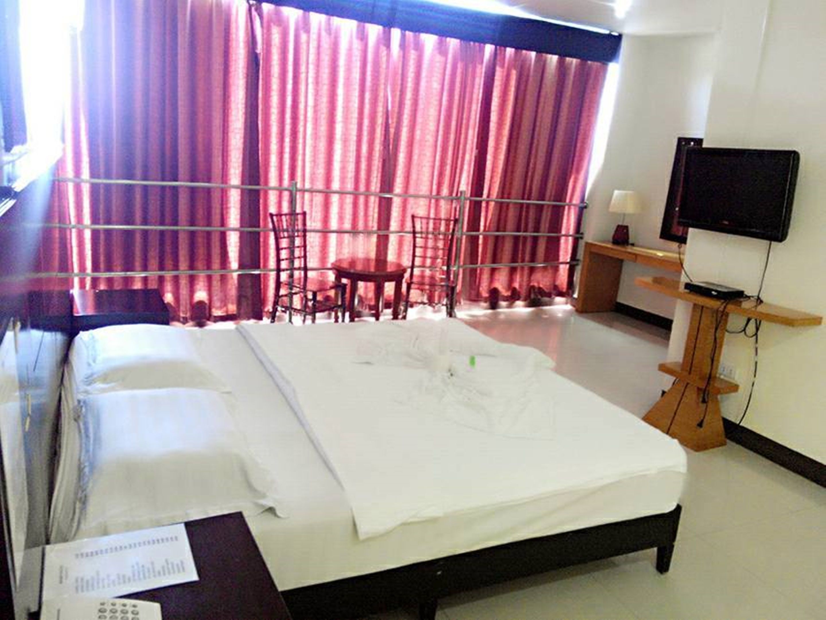 A hotel room with a bed, a desk, a chair, a TV, and a window with curtains.