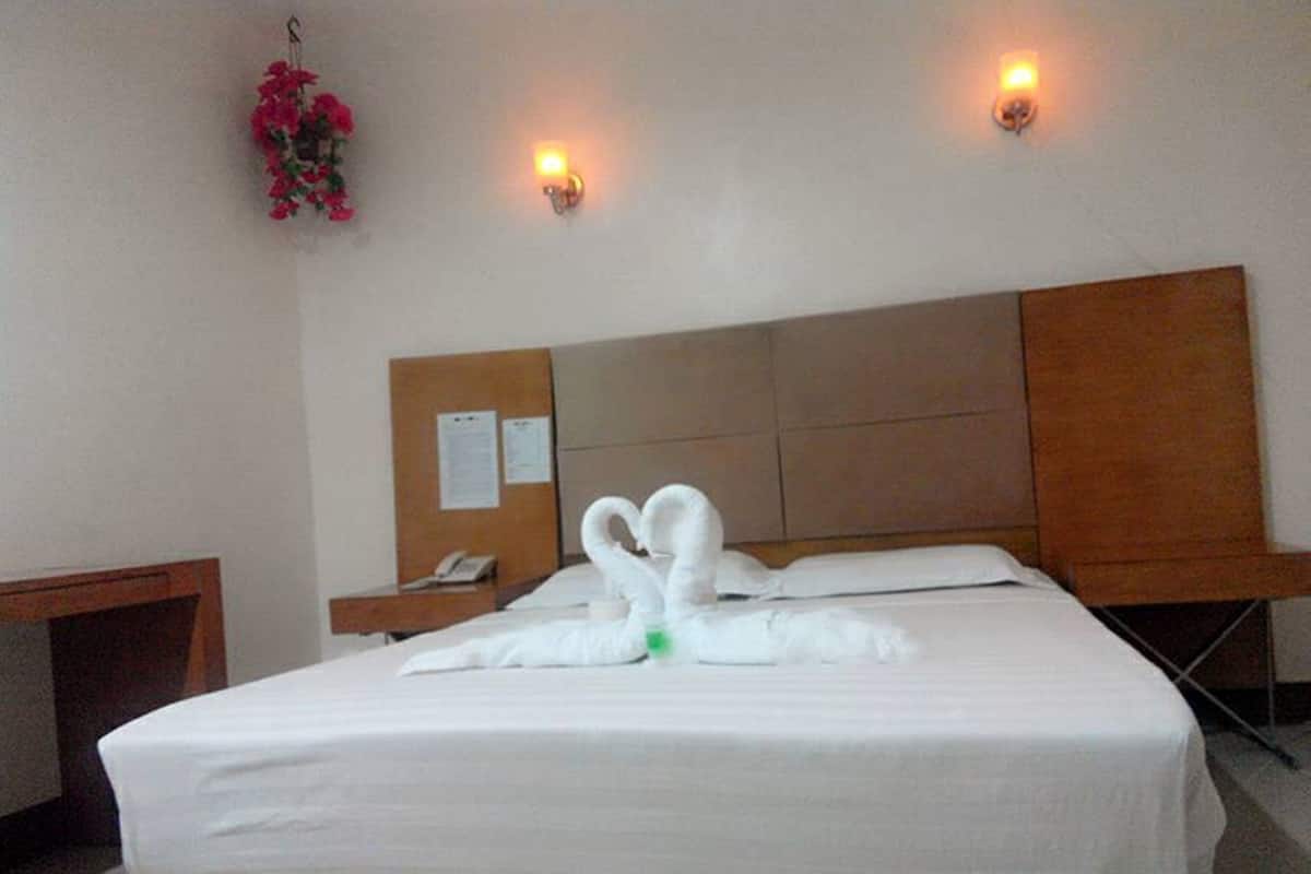 Une chambre d’hôtel avec un lit bien fait, une tête de lit en bois, une table de chevet avec une lampe et un téléphone fixé au mur.