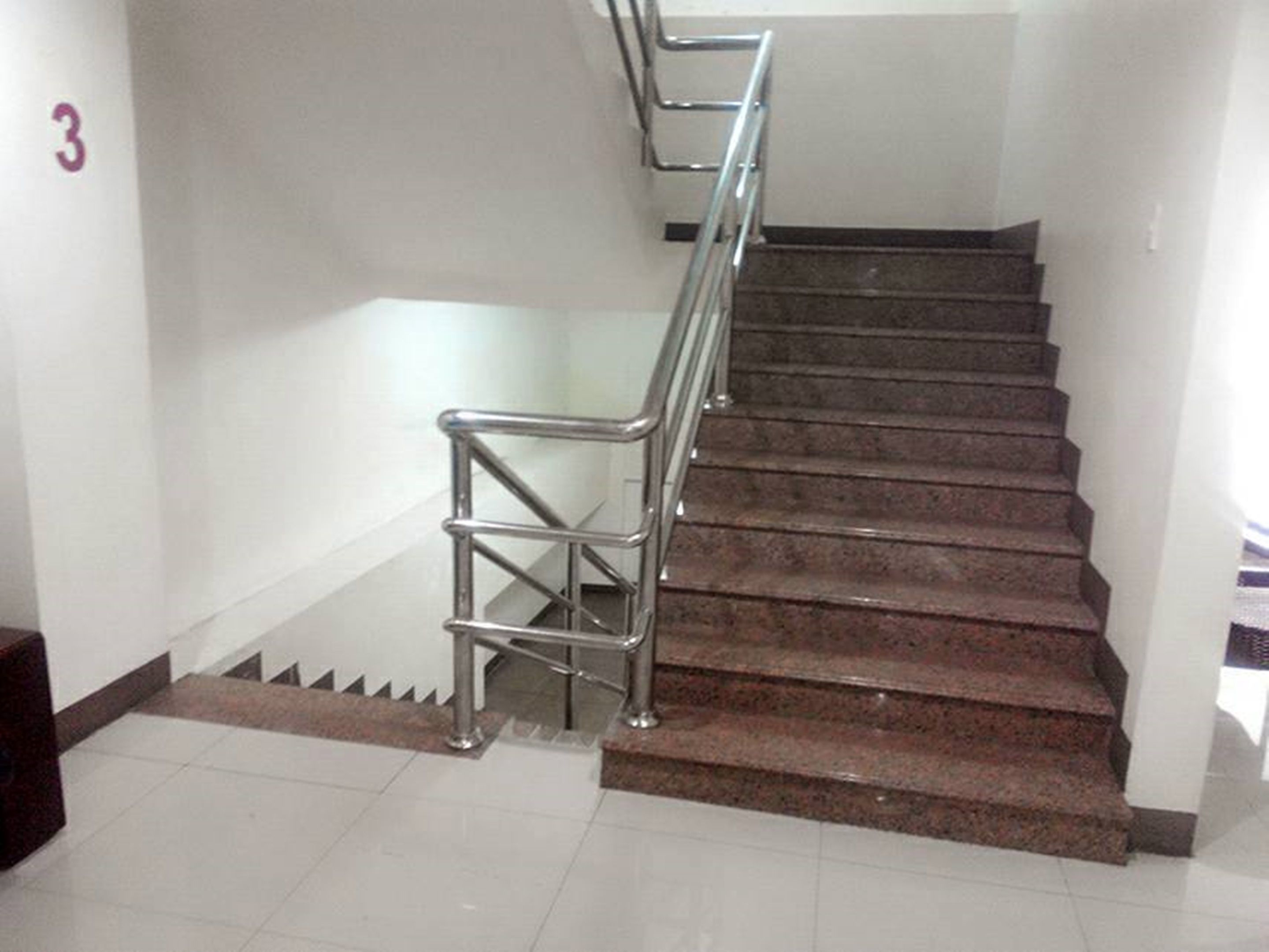 A staircase with metal handrails, carpeted steps, and a white tiled floor.