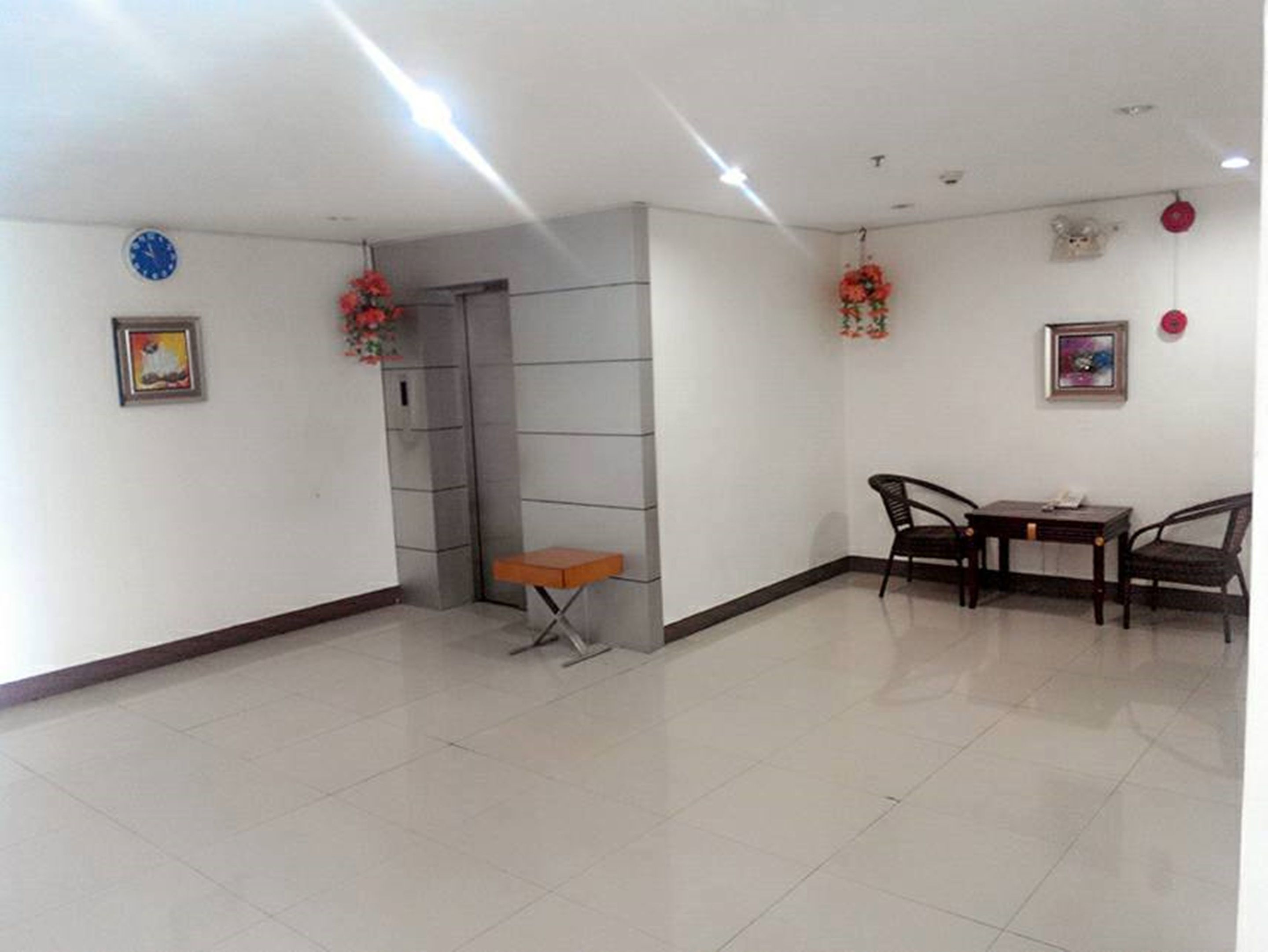 Una habitación con piso de baldosas, una mesa pequeña con sillas, un reloj en la pared y un cuadro enmarcado.