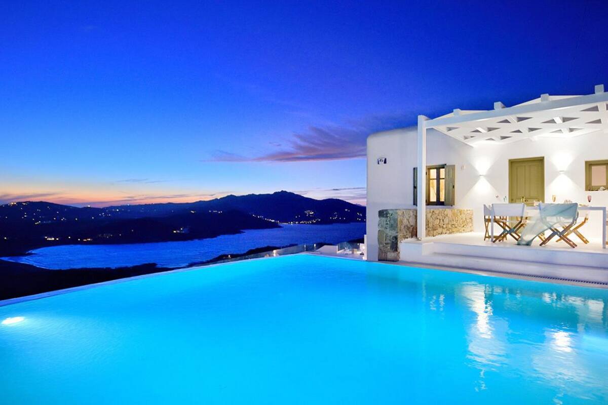 A poolside area with a view of the sea and mountains at dusk.
