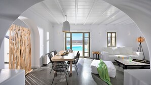 A modern interior with a dining area, a sofa, and a view through large windows.
