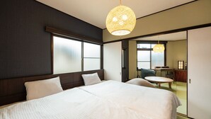 A hotel room with a large bed, a desk, and a chair. There are two windows and a hanging light fixture. - Shiori (Kyoto)