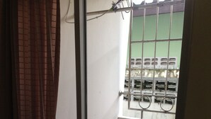 Un balcón pequeño y cerrado con suelo de baldosas, una ventana con rejas y un extintor de incendios en la pared.