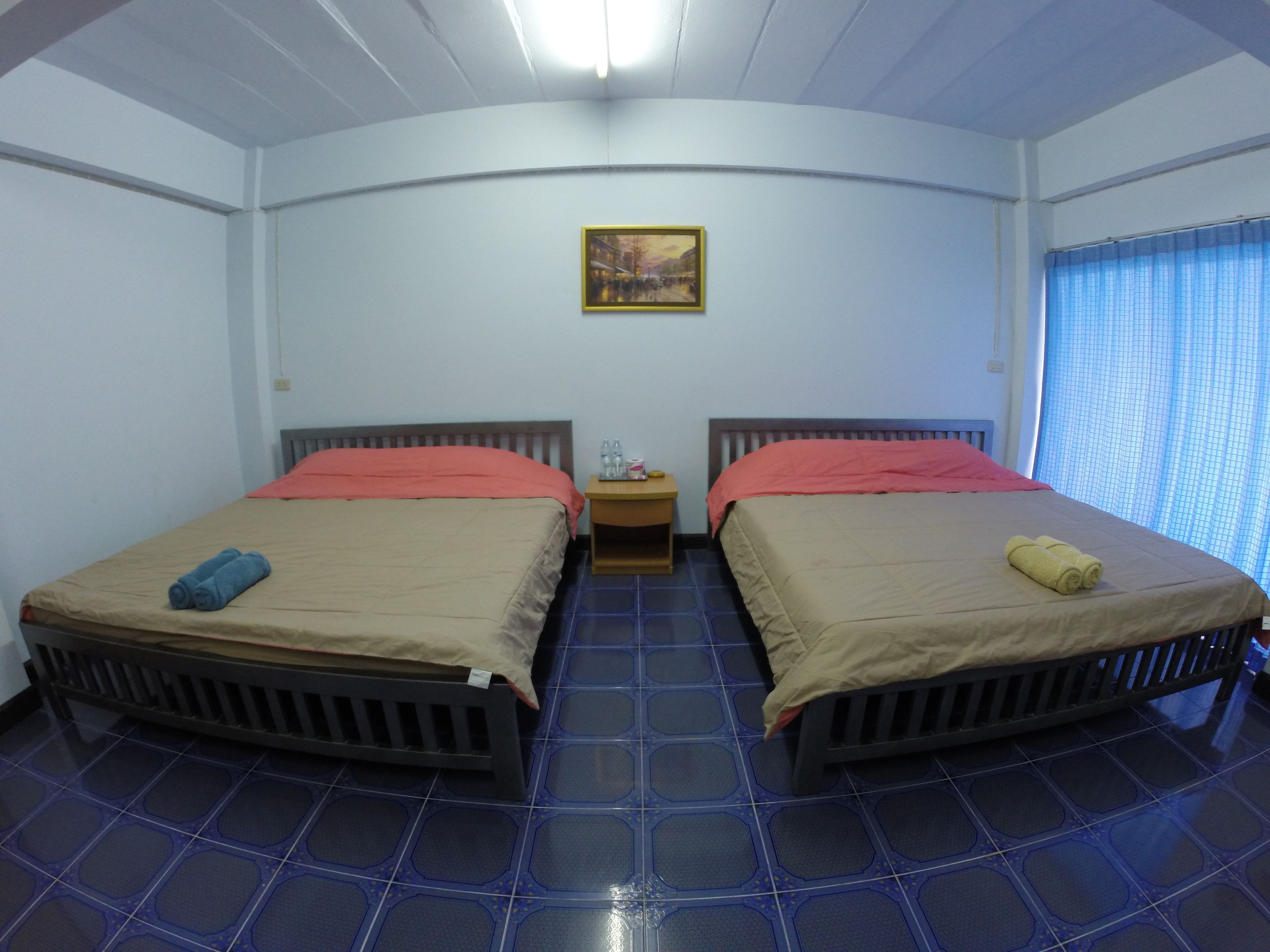 Una habitación con dos camas, una mesita de noche, un cuadro en la pared y una ventana con cortinas.