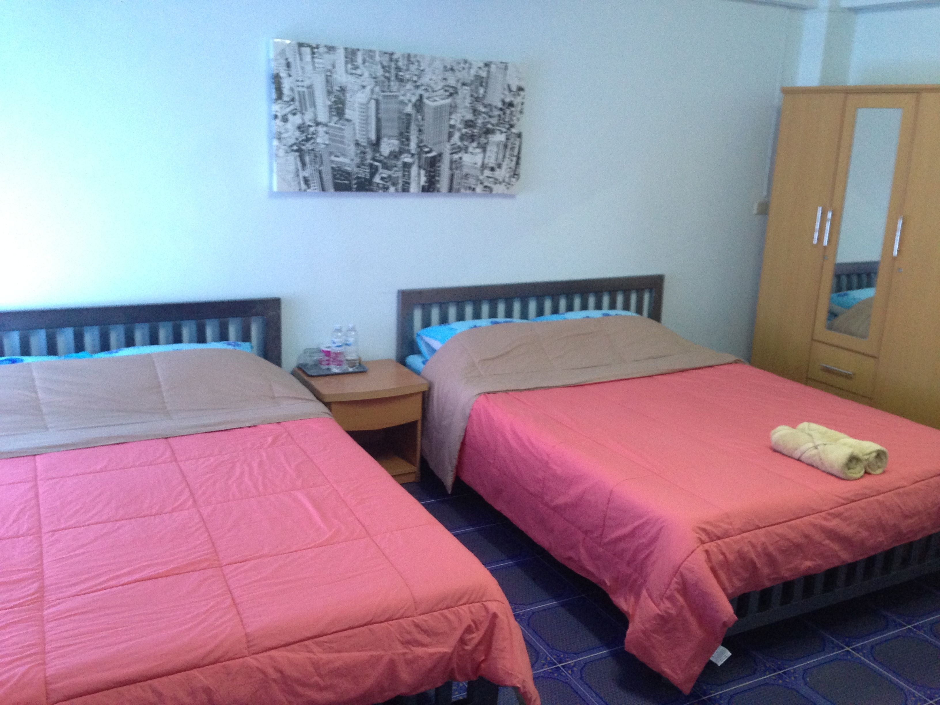 Een hotelkamer met twee bedden, een nachtkastje, een garderobe en een stadsgezichtschilderij aan de muur.