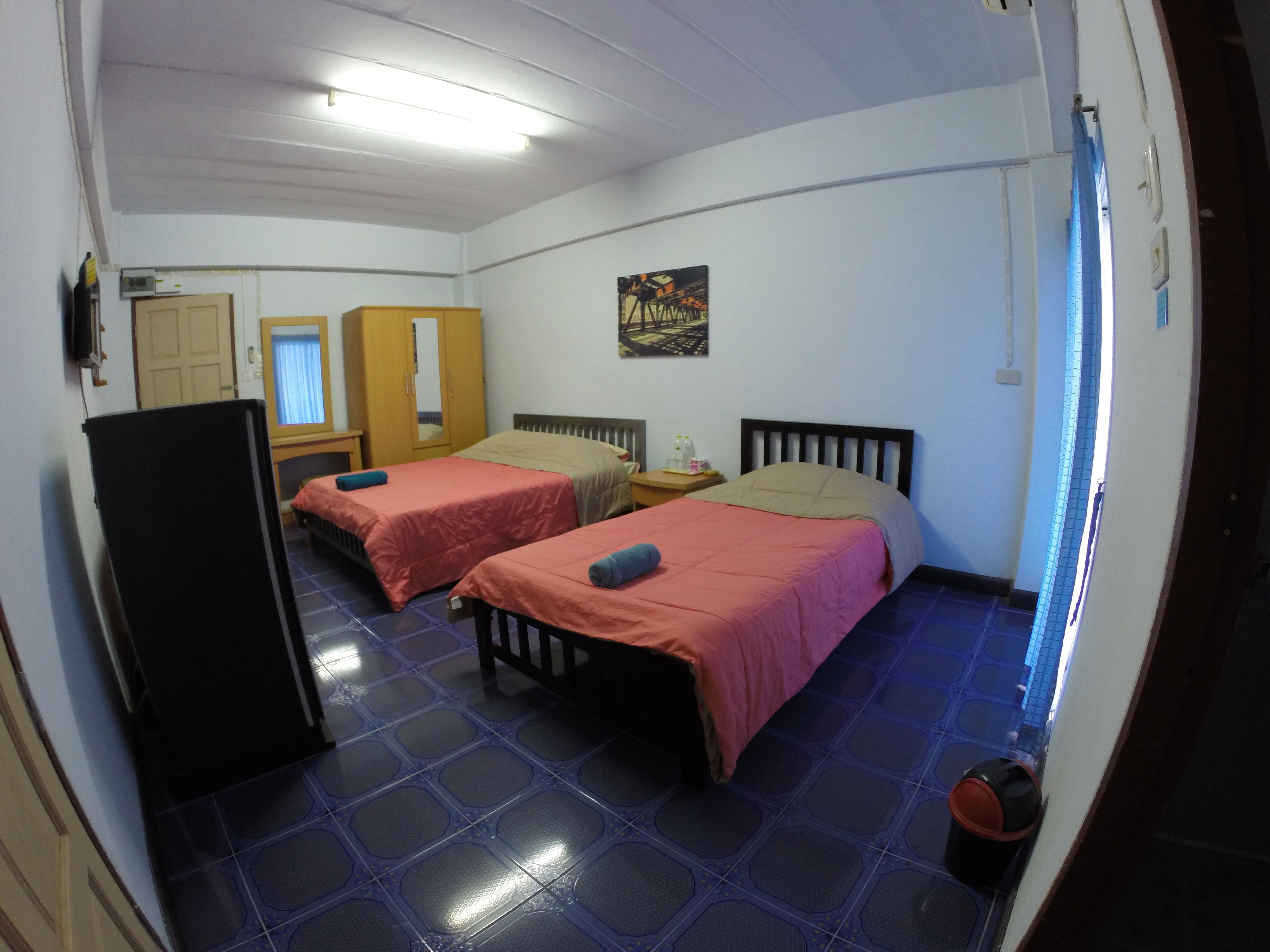 A room with two beds, a wardrobe, a small table, and a refrigerator.