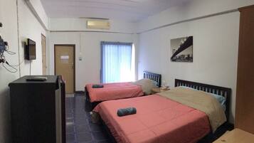 A room with two beds, a desk, a television, and a window with curtains.