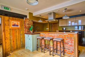 A kitchen with a brick island, bar stools, a sink, and modern appliances. - Easton Guest House (Norwich)