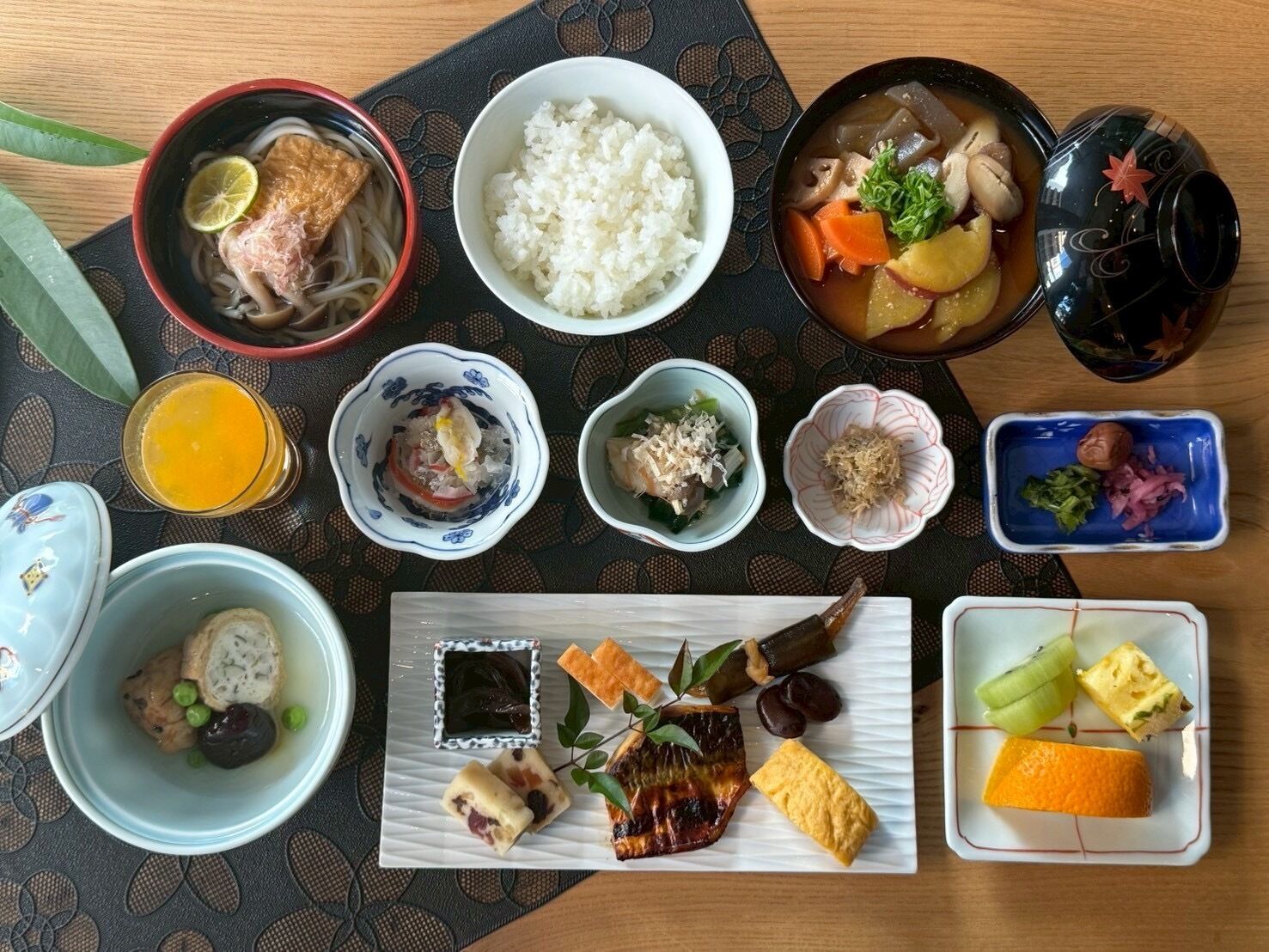 A variety of Japanese dishes including rice, soup, and sashimi, arranged on a table with a patterned placemat.