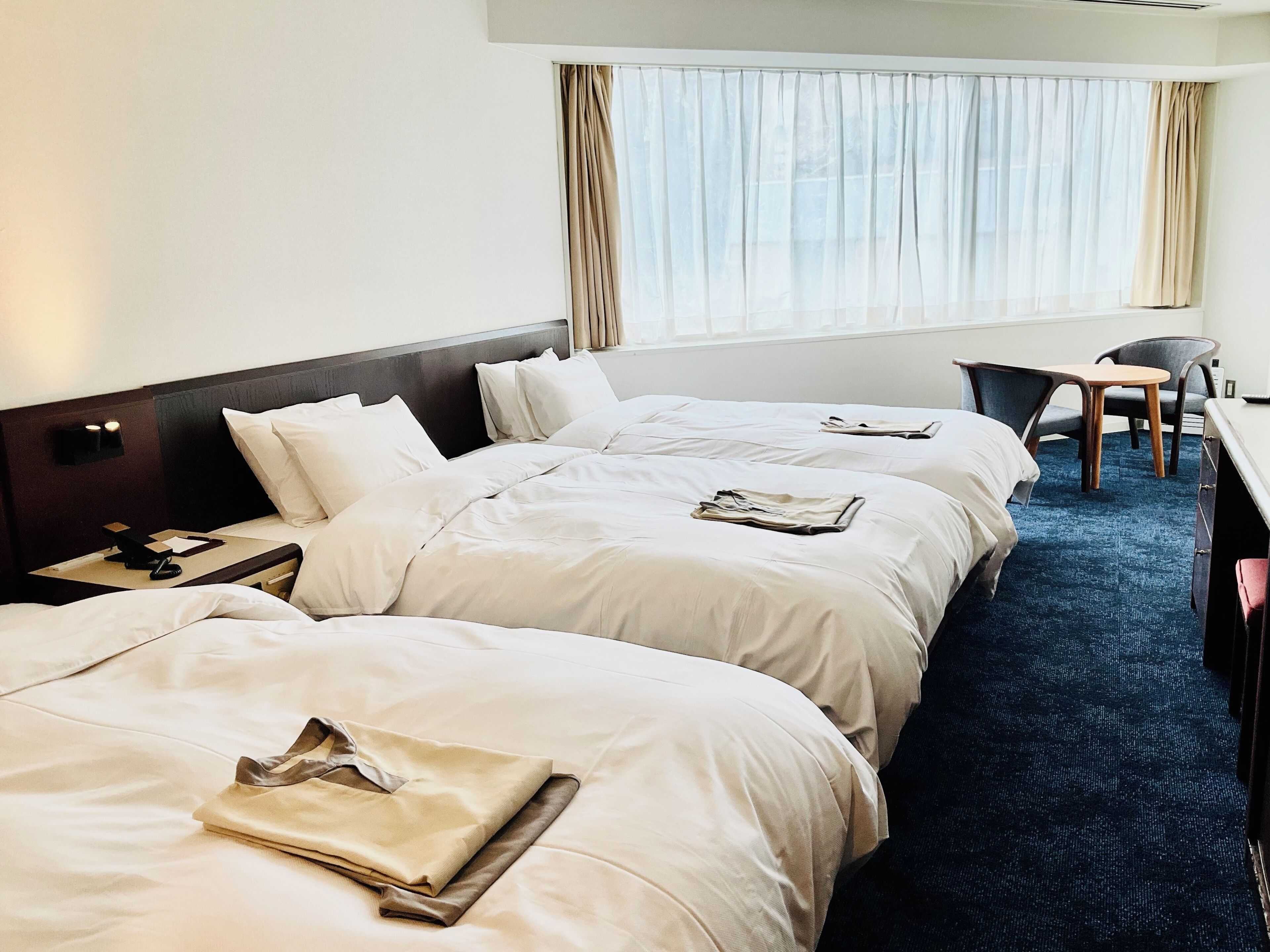 A hotel room with three beds, a desk, and a chair.