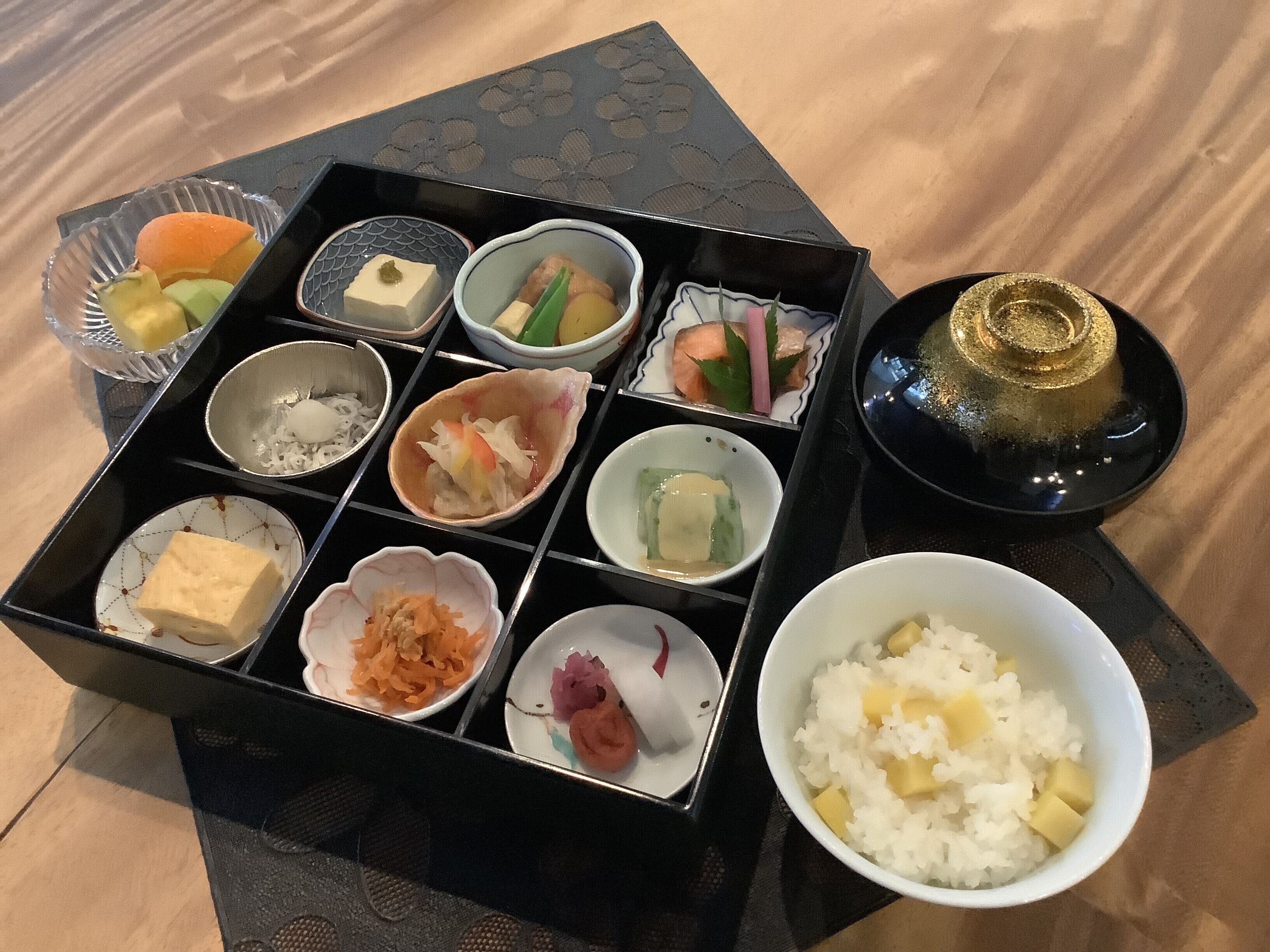 A traditional Japanese bento box with various food items and a bowl of rice.